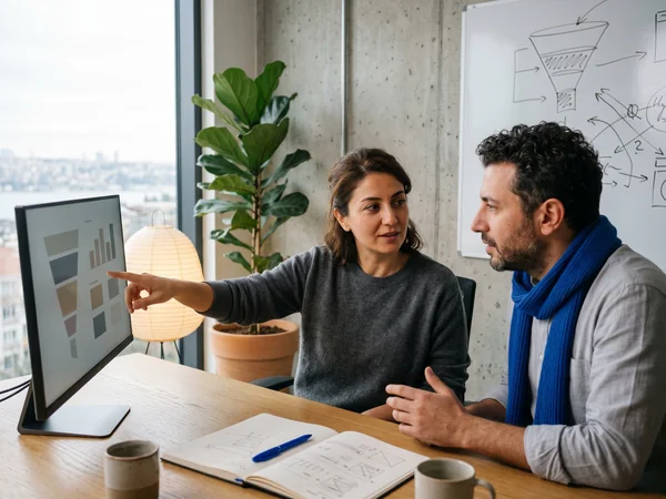 Two senior CRO strategists collaborating at a whiteboard covered in funnel diagrams and hypotheses.